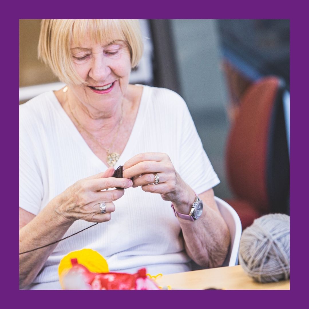 A lady smiling as she knits.