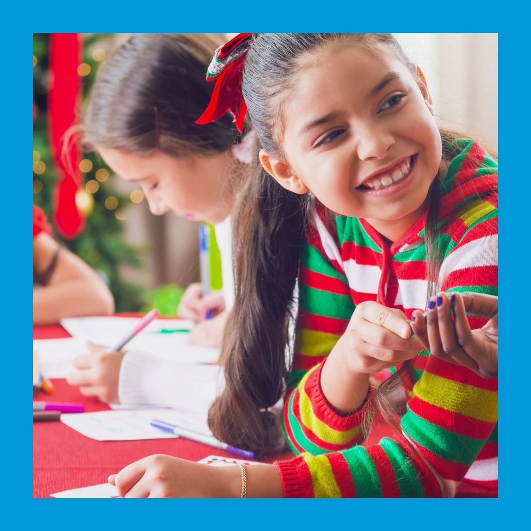 A photo of two girls working at a craft table with a Christmas tree in the background