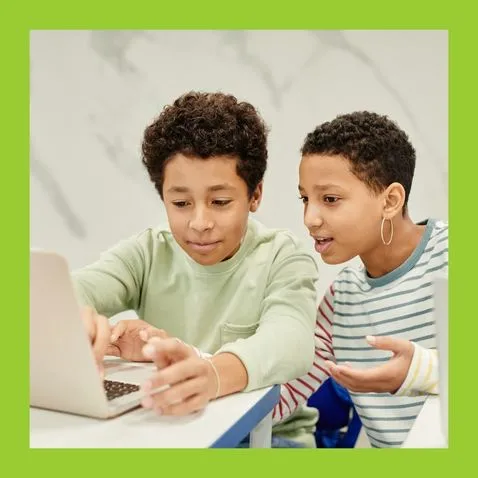 A photo of a young woman helping a boy with his laptop