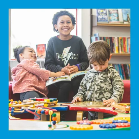 A child and two toddlers enjoy books and tabletop manipulatives in a library