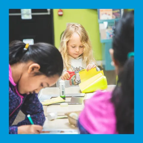 Three children work on crafts and colouring around a table