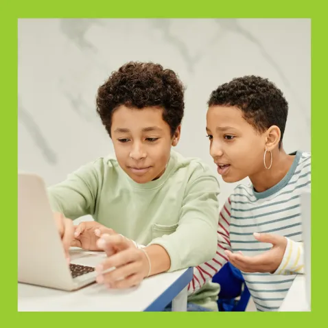 And adult and child sat at a laptop, the adult is calmly explaining something to the child