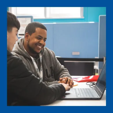 A photo of a man wearing a lanyard helping another man with his laptop
