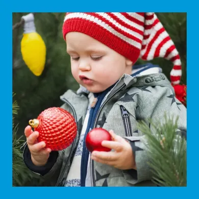 A photo of a toddler in a red and white striped hat holding a plastic christmas ball in each hand