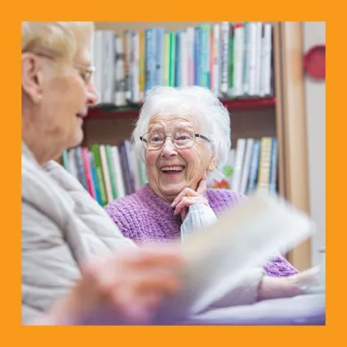A woman smiling at another woman holding a book.